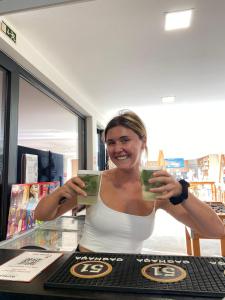 a woman is holding up two green drinks at WOT Ericeira Surf Hostel in Ericeira