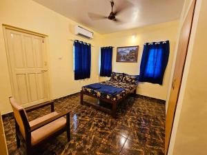 a room with a bed and a chair and blue curtains at Casa de Bella in Candolim