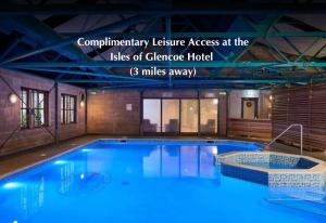 a large swimming pool with blue water in a building at Forest Corner Luxury Home with Hot Tub in North Ballachulish