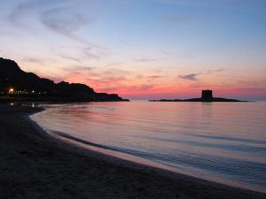 a sunset on the beach with a lighthouse in the distance at UNAHOTELS Club Hotel Ancora in Stintino