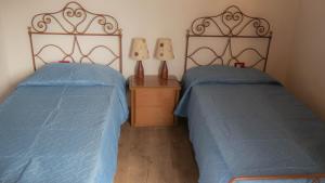 two beds in a bedroom with blue sheets and two lamps at Sa domo 'e su furru in Codrongianos