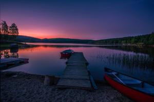 a dock with a boat on a lake at sunset at Rödvattnet cottages in Rödvattnet