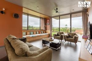 a living room with a couch and chairs and windows at StayVista at Terracotta Skies with Courtyard & Pool in Nashik