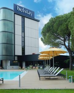 a hotel with benches and umbrellas in front of a pool at Belstay Venezia Mestre in Marghera