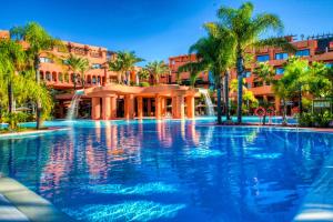 a large swimming pool with palm trees and a building at Royal Hideaway Sancti Petri in Chiclana de la Frontera