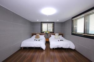 a bedroom with two beds with white sheets and two windows at Uljin Blue Ara CD pension in Uljin