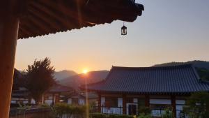 a building with a roof with the sun in the background at Boseong Greenery Hanok Pension in Boseong