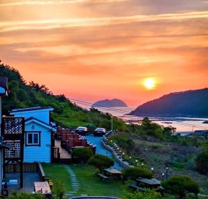 a sunset view of a road with a house and the ocean at Jeonnam Cheongsando Yeohaeng Pension in Wando