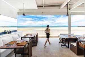 a woman walks through a restaurant with a view of the beach at Putahracsa Hua Hin in Hua Hin