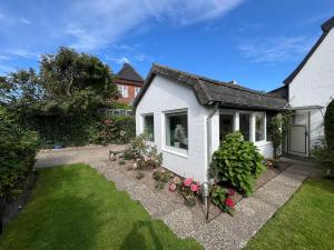 ein kleines weißes Haus mit Blumen im Hof in der Unterkunft Zur Himmelsleiter in Westerland