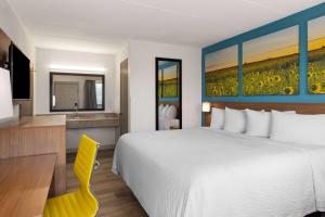 a hotel room with a bed and a desk and a sink at Day's Inn & Suites by Wyndham Indianapolis Airport East in Indianapolis +23 photos