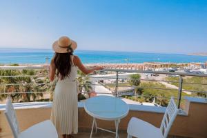 a woman in a hat standing on a balcony looking at the ocean at Sole Luna Hotel in Borsh