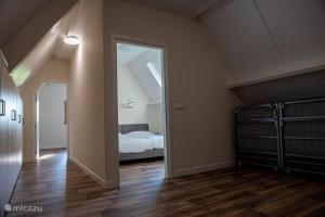 an attic room with a bed and a hallway with a doorway at Erve Schuurboer in Tilligte