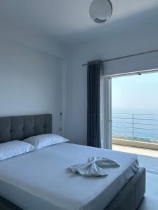 a bedroom with a white bed with a large window at Vila Jona Palasë in Dhërmi