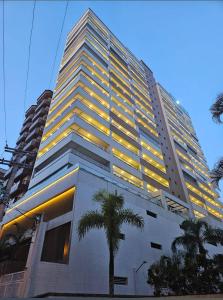 a tall building with a palm tree in front of it at Linda Cobertura vista mar no Residencial Affinity in Praia Grande