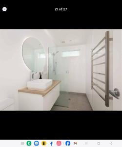 a white bathroom with a sink and a mirror at Waihi beach Toroha cosy cabin in Waihi Beach