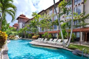 a hotel pool with lounge chairs and palm trees at Prime Plaza Hotel Sanur – Bali in Sanur