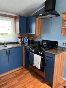 a kitchen with blue cabinets and a stove top oven at Place2bee,Family & Pet Friendly 6 Berth Caravan, Manor Park Hunstanton in Hunstanton