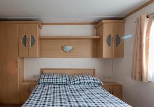 a bed in a small room with wooden cabinets at Carnaby Holiday Caravan, West Sands, Selsey in Selsey