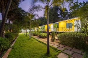 a yellow house in a garden with palm trees at Nathan Resort with Swimming Pool in Puducherry