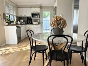 a kitchen with a table with chairs and a vase with flowers at Little Avalon House in Whale Beach
