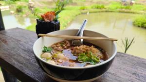 a bowl of soup on a table with a view of a river at Rimna Banpark 2 ริมนาบ้านพัก2 in Ban Sop Mae Klang