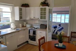 cocina con armarios blancos, mesa y fogones en Victorian Beachfront Apartment with Ocean Views - The Coachhouse, en Narrabeen