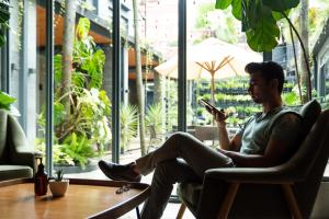 a man sitting in a chair looking at his cell phone at Nomad Hotel in Kathmandu