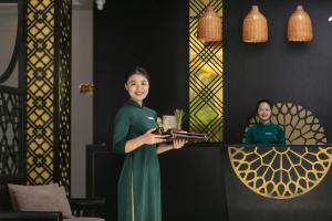 a woman in a green dress holding a tray of wine glasses at Hoi An Golden Holiday Villa in Hoi An