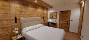 a bedroom with a white bed and a wooden wall at Hotel Corona Ferrea in Sappada