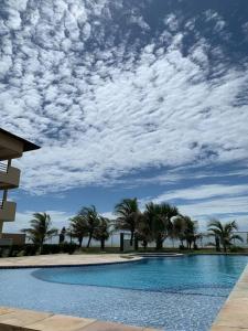 a swimming pool with palm trees and a cloudy sky at Flat Marezzi - Pé na areia - Taíba CE in São Gonçalo do Amarante