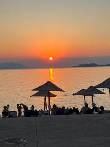 a group of people sitting on the beach watching the sunset at Loutraki comfortable apartment center 50m from the sea in Loutraki