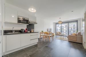 a kitchen with white cabinets and a living room at L'Ambre - T2 Lumineux - Parking, RER A, Disneyland in Montévrain