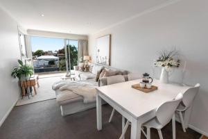 a white living room with a table and a couch at Mount Maunganui Beach Apartment in Mount Maunganui