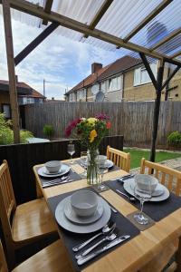 Una mesa de madera con platos y un jarrón de flores encima. en EcuaStay New Luxurious 4 Bedroom Home with Garden and parking, en Dagenham