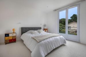a white bedroom with a bed and a large window at Maison et jardin, 600m de la mer, St Brevin in Mindin