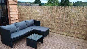 a couch on a patio with a table and a fence at The Steps Holiday Let PHOCLE GREEN ROSS-ON-WYE HR9 7TW in Crow Hill