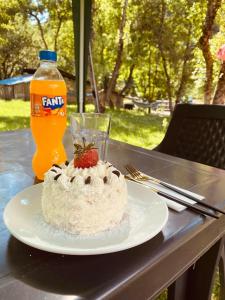 a cake on a plate on a table with a bottle of orange soda at Guest House Mariami in Ushkhvanari