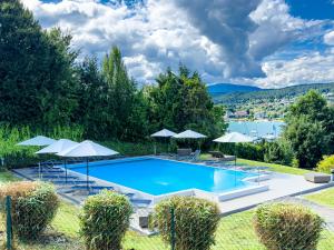 a swimming pool with chairs and umbrellas at Avío, 2 Bedroom, Terrace, private lake Access in Velden am Wörthersee