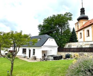 a white house with a black roof and a church at Relax apartmány na statku u Orlické přehrady in Klučenice