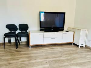 a flat screen tv sitting on a white cabinet with black chairs at Descubre Cantabria 2! A 4 minutos de Cabárceno y capacidad para 6 adultos! in Sarón
