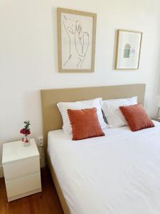 Un dormitorio con una cama con sábanas blancas y almohadas naranjas. en Vila Olivença, en Costa da Caparica