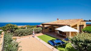 a house with a yard with chairs and an umbrella at Villa Vincent in Costa Paradiso
