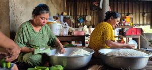two women are preparing food in large metal bowls at Tonle Mekong Homestay in Krong Kracheh