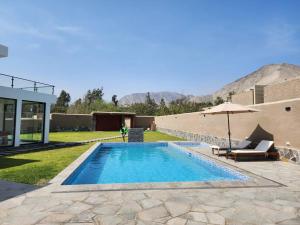 a swimming pool with an umbrella next to a house at Casa de campo de estreno en Cieneguilla, Lima-Perú in Cieneguilla