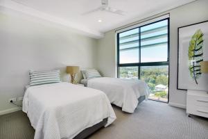two beds in a white room with a window at Absolute Kirra by EcoTime in Gold Coast
