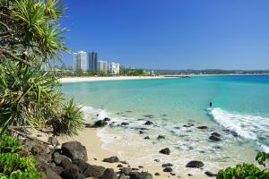 a beach with a person surfing in the ocean at Absolute Kirra by EcoTime in Gold Coast