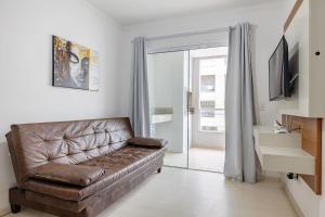 a living room with a brown leather couch and a television at Excelente Apartamento a 2 minutos da Praia de Bombas in Bombas