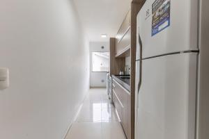 a white kitchen with a refrigerator and a hallway at Excelente Apartamento a 2 minutos da Praia de Bombas in Bombas