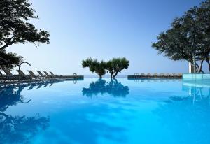 a pool of blue water with chairs and trees at Kakkos Bay Hotel and Bungalows in Ierápetra